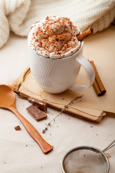 Cup of cocoa with cinnamon, whipped cream and chocolate. Textile background. Scandinavian winter concept. Vertical composition. - 写真・画像