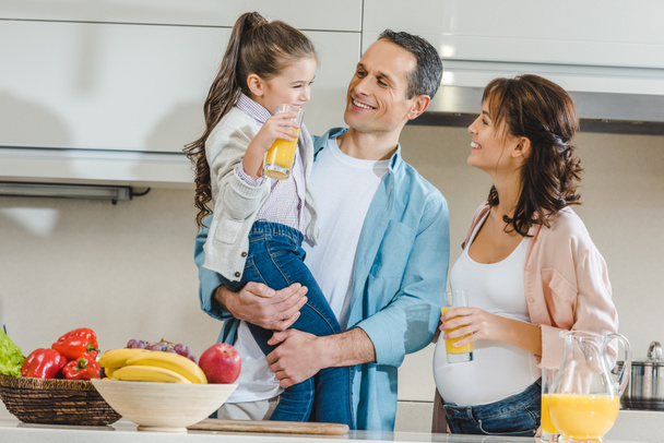 familia feliz con jugo, verduras y frutas en la cocina mirándose unos a otros
 - Foto, Imagen