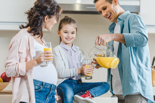 happy family, father pouring juice in glass for daughter at kitchen - Foto, afbeelding