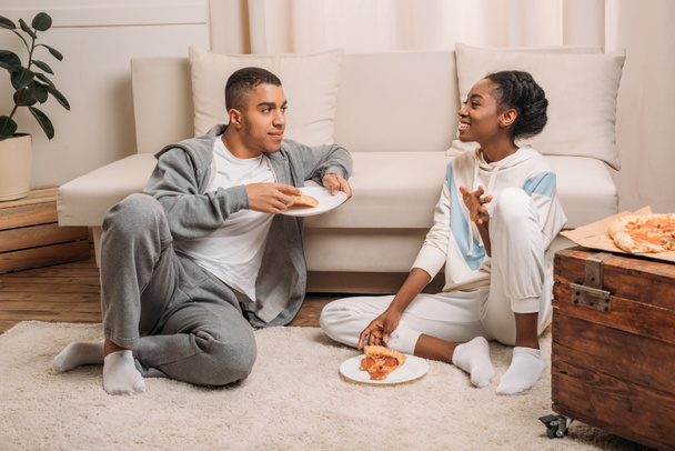 couple eating pizza beside sofa - 写真・画像