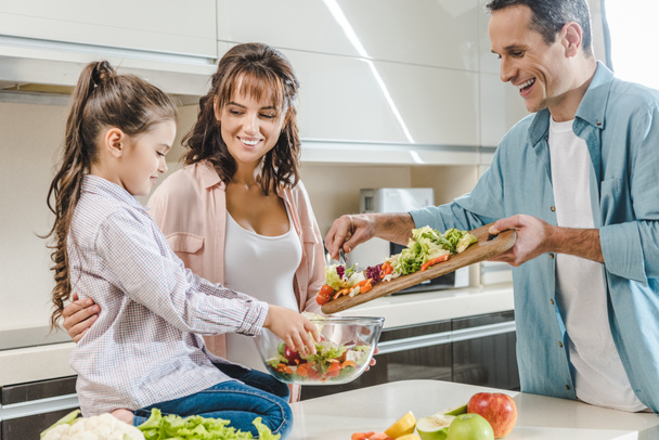 happy smiling family making salad together at kitchen  - Photo, Image