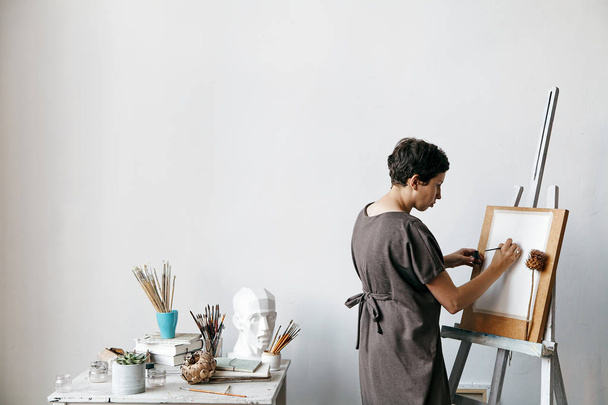Female artist in her spacious white studio working with watercolor painting.  Natural lighting. Disclosure of creativity concept. Horizontal composition with copy space. - 写真・画像