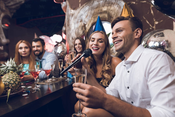 Young people are resting in a trendy nightclub. A guy in a white shirt and a girl in a black dress are singing. - Photo, Image