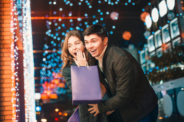 Счастливая пара с пакетами для покупок наслаждается ночью на фоне города
 - Фото, изображение