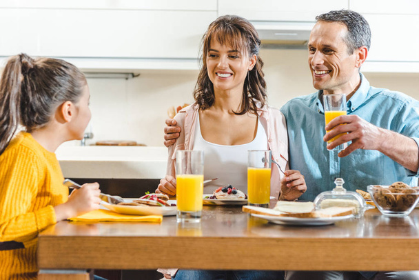 cheerful family sitting at table and holding glasses with juice at kitchen - Фото, зображення
