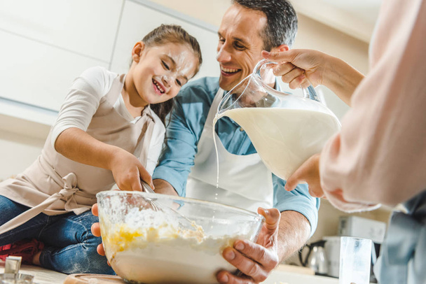 cropped image of female hands pouring milk in bowl when father and daughter mixing dough - Foto, Imagen