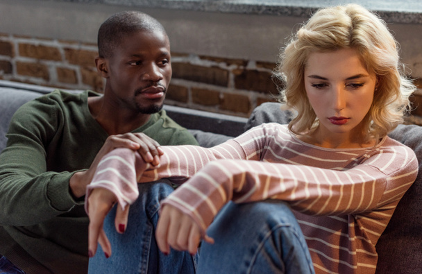 african american man looking at upset girlfriend while sitting on sofa at home, relationship problems concept - Photo, Image