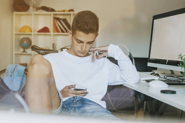 tiener of jonge man student op het bureaublad met de mobiele telefoon en computer - Foto, afbeelding