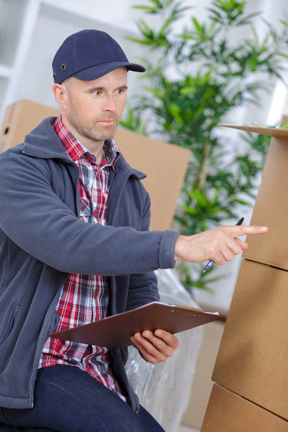 cheerful young man mover holding a cardboard boxes - Foto, Bild