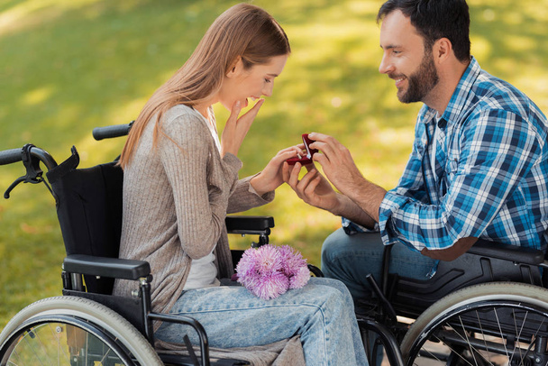 A man and a woman in wheelchairs met in the park. A man makes a woman a prepossess. - Fotoğraf, Görsel