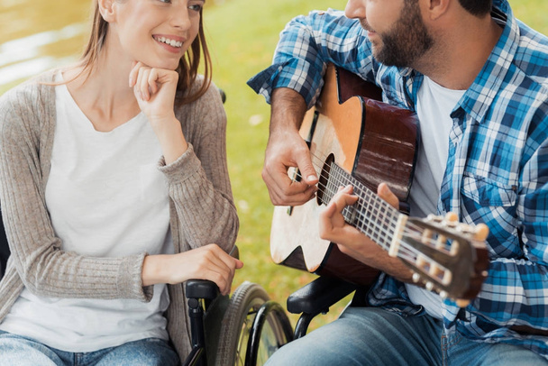 A man and a woman in wheelchairs met in the park. A man is playing the guitar, the woman listens and smiles. - Foto, Bild