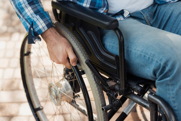 Close up. A disabled man in a wheelchair holds hands behind the wheelchair wheels. - Foto, immagini