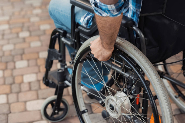 Close up. A disabled man in a wheelchair holds hands behind the wheelchair wheels. - 写真・画像