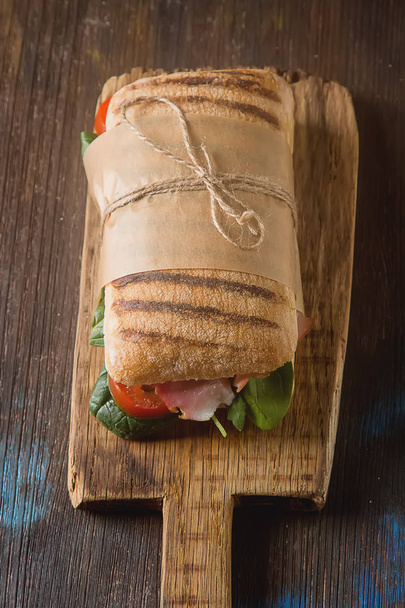 French baguette with sausage, tomatoes and lettuce. Dark backgro - Photo, image