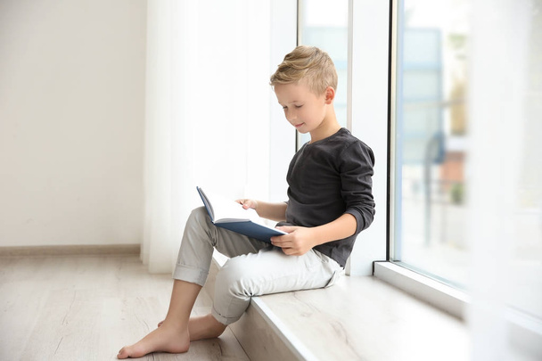 Cute little boy reading near window at home - Foto, Bild