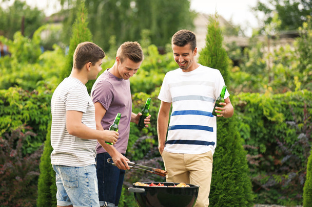 Men cooking tasty food on barbecue grill, outdoors - Foto, imagen