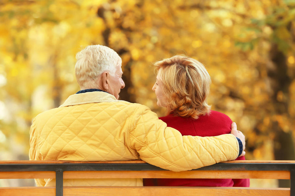 Elderly couple sitting on bench in autumn park - Photo, image