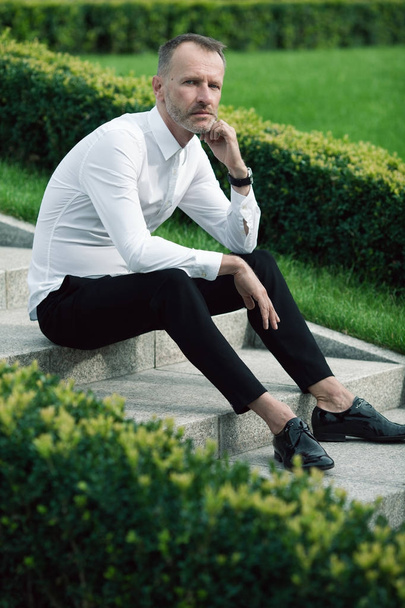 Luxurious and stylish concept. Rich mature man sitting on marble stairs - Photo, image