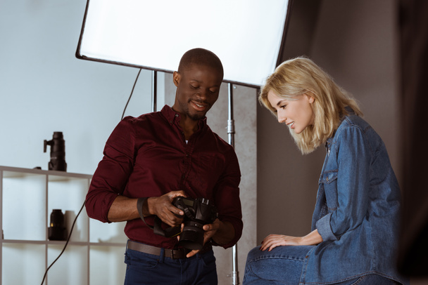 african american photographer and caucasian model choosing photos together during photoshoot in studio - Photo, Image