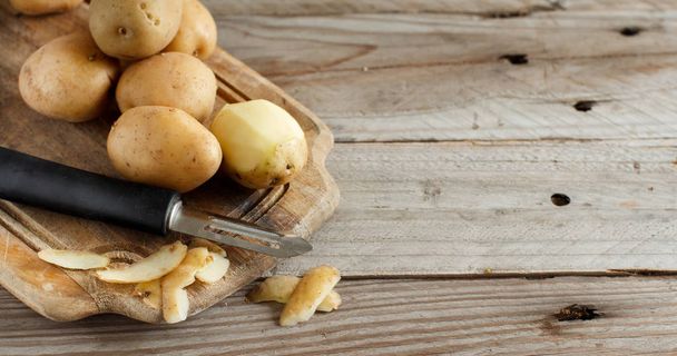 Raw potatoes with a vegetable peeler - Foto, Imagen