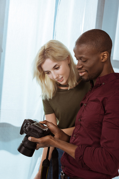 portrait of african american photographer and caucasian model choosing photos together during photoshoot in studio - Photo, Image