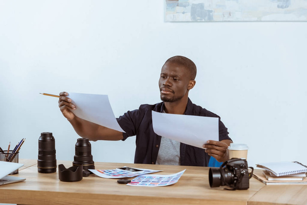 portrait of focused african american photographer looking at photoshoot examples at workplace - Foto, imagen