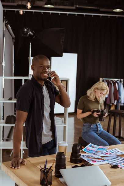 fotógrafo americano fican falando no smartphone enquanto colega caucaisan escolher fotos em estúdio
 - Foto, Imagem