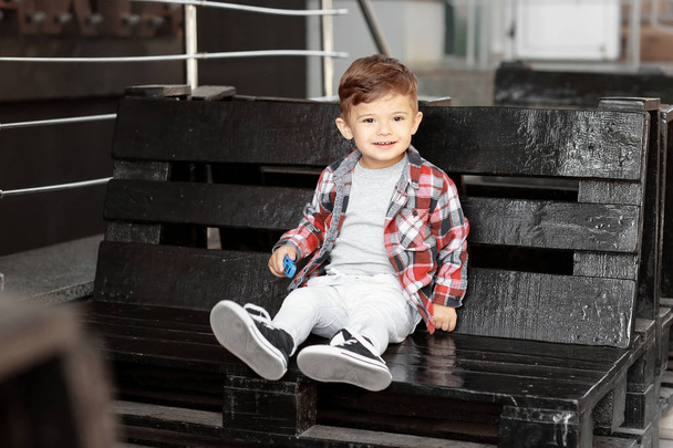 Очаровательный маленький мальчик сидит на скамейке в открытом кафе
 - Фото, изображение