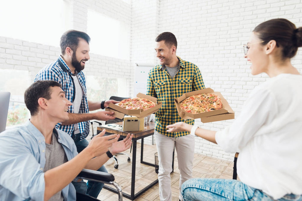 Office workers and man in a wheelchair are eating pizza. They work in a bright and modern office. - Foto, Bild