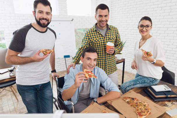 Office workers and man in a wheelchair are eating pizza. They work in a bright and modern office. - Foto, afbeelding