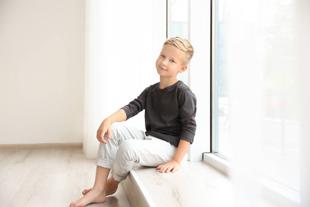 Симпатичный маленький мальчик сидит у окна дома
 - Фото, изображение
