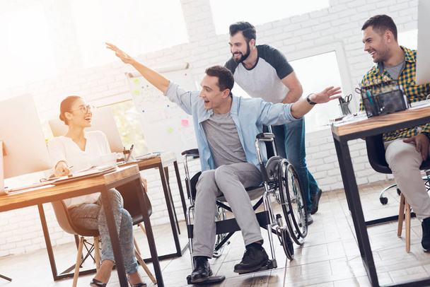 A colleague rolls a person in a wheelchair around the office. They have fun and laugh. - Foto, Imagen
