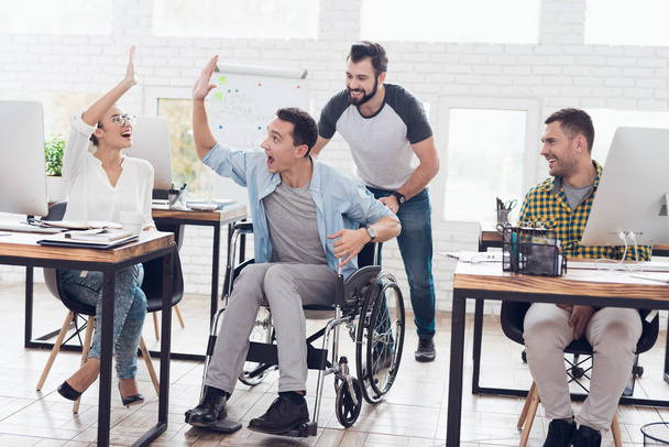 A colleague rolls a person in a wheelchair around the office. They have fun and laugh. - Φωτογραφία, εικόνα