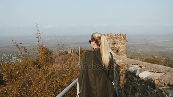Młoda kobieta turystycznych w zieloną skórzaną kurtkę spacery muru twierdzy starożytnego zamku. Strzał w zwolnionym tempie 100fps - Materiał filmowy, wideo