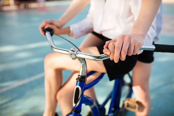 Foto de cerca de cuerpos de hombres y mujeres jóvenes montando juntos en bicicleta azul. Foto de manos de hombre y mujer sosteniendo manillar de bicicleta
 - Foto, Imagen