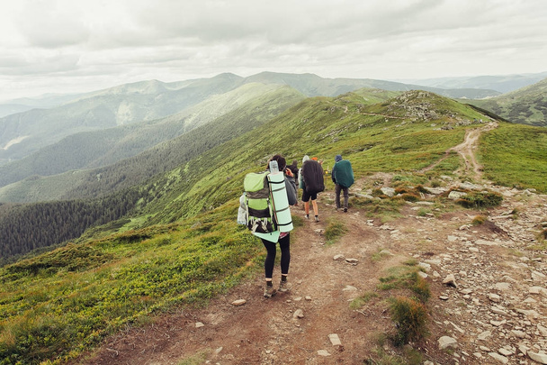 Group of hikers with backpacks walk along a trail towards a mountain ridge - Foto, imagen