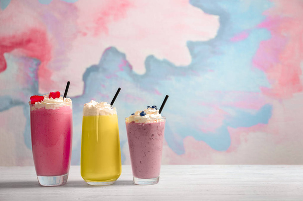 Different milkshakes in glasses on table against color background - 写真・画像