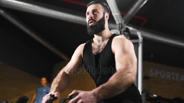 Strong man is pumping muscles at the gym, strength exercises on simulators, athlete at fitness club, caucasian man with beard is pumping muscles - Felvétel, videó