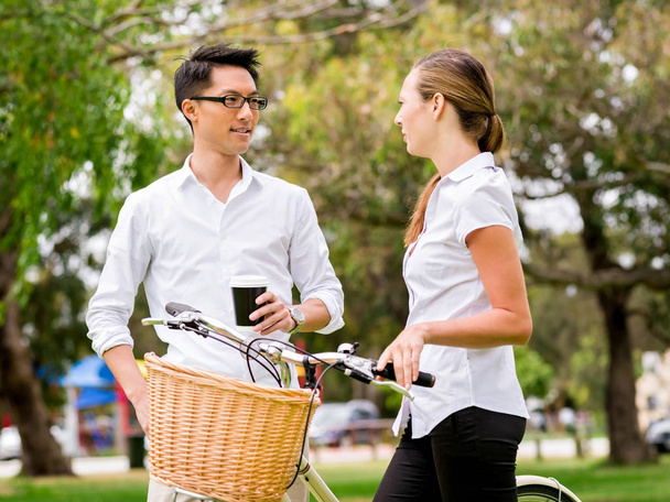 Portrait of smiling couple standing in park with bike talking - Photo, image