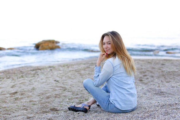 Hymyilevä nuori nainen lepää rannalla ja poseeraa kameran edessä, istuu
 - Valokuva, kuva