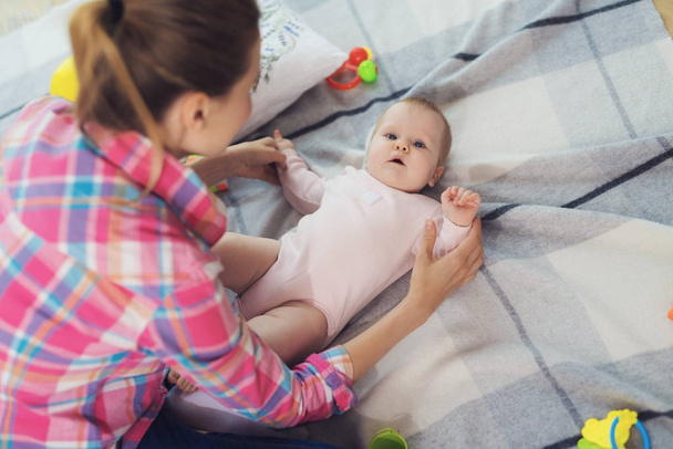 Eine Frau in rosa Hemd sitzt auf dem Fußboden im Wohnzimmer und spielt mit ihrem kleinen Kind. Kind spielt wirklich gerne. - Foto, Bild