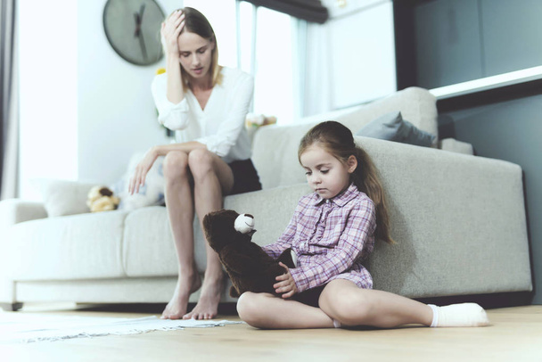 La femme parle à une petite fille offensée, qui s'assoit à côté du canapé et tient un jouet dans ses mains
. - Photo, image