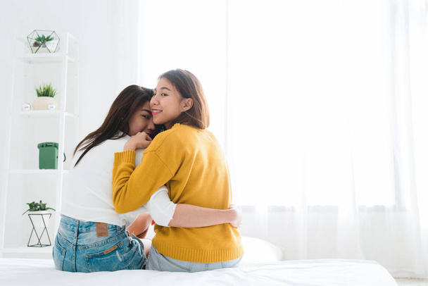 Back view of women lesbian happy couple waking up in morning, sitting on bed, stretching in cozy bedroom, looking through window. Funny women after wakeup. Lesbian couple together indoors concept. - Фото, изображение