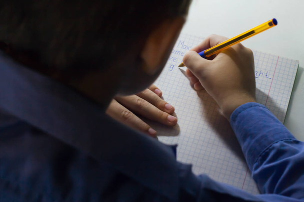 Zbliżenie dłoni chłopca ołówkiem, pisanie słów angielskich ręcznie na tradycyjny biały notatnika papieru. - Zdjęcie, obraz