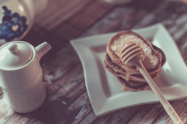 Delicious breakfast. Homemade Pancakes with honey and cup of tea on wooden rustic background table. Vintage style retro toned image - Фото, изображение