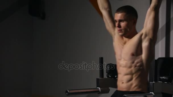 a man with a naked torso sit-UPS with leg raises on the horizontal bar in the gym. - Video