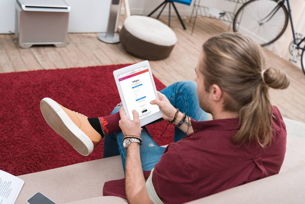 man sitting on sofa while using digital tablet with instagram appliance - Foto, Imagem