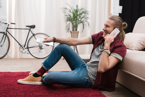 handsome man talking on smartphone while watching tv at home  - Foto, Imagen