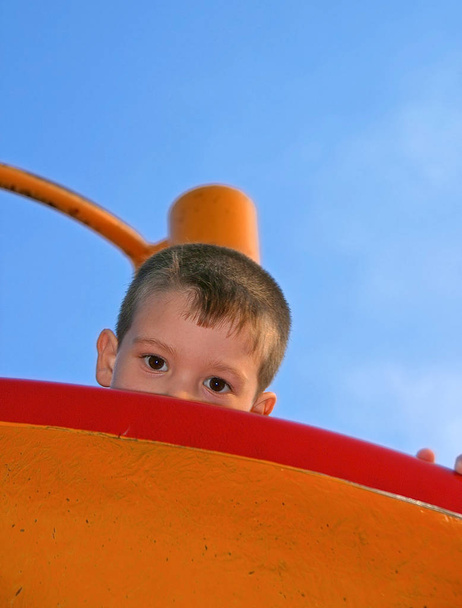 színes és kontrasztos képet, egy kisfiú, aki bujkál a játszótér játék közben. Vicces képek. - Fotó, kép