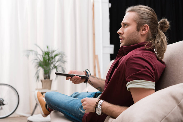 красивый сконцентрированный мужчина с пультом дистанционного управления смотрит телевизор дома
  - Фото, изображение